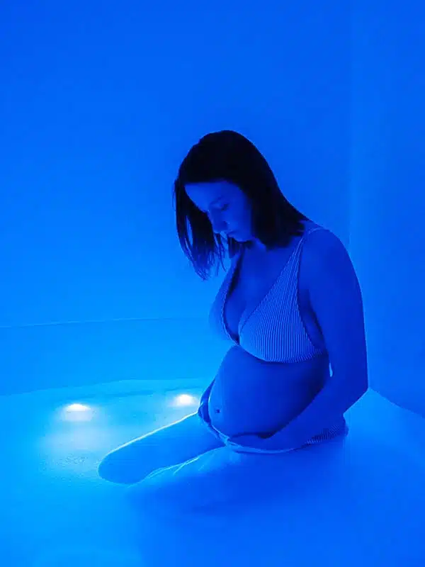 Pregnant woman kneeling in an Ocean Float Room flooded with soft blue light