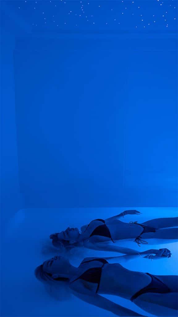 Couple floating in a tall, walk-in float tank with star-like ceiling lights