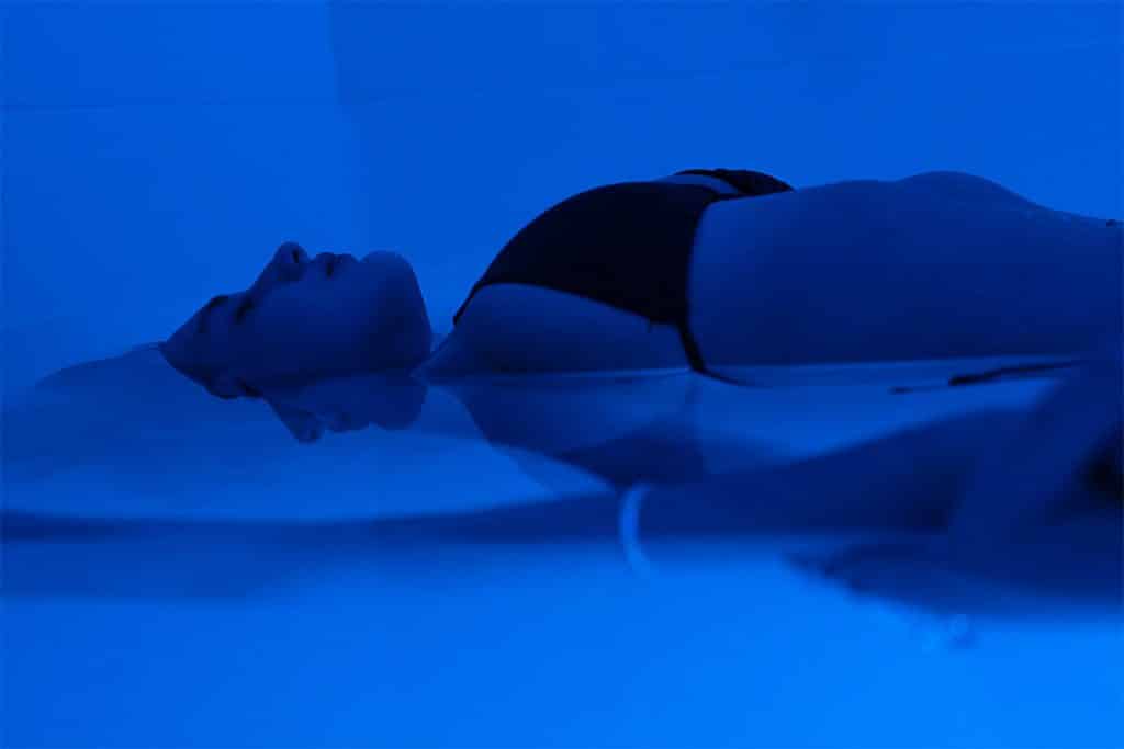 Person floating calmly in a floatation therapy room, resting on saltwater in low light